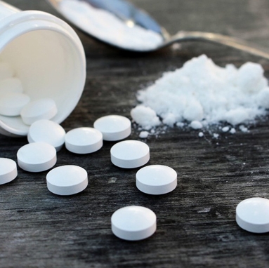 Spoon with ground up pills, bottle spilled with whole pills on table