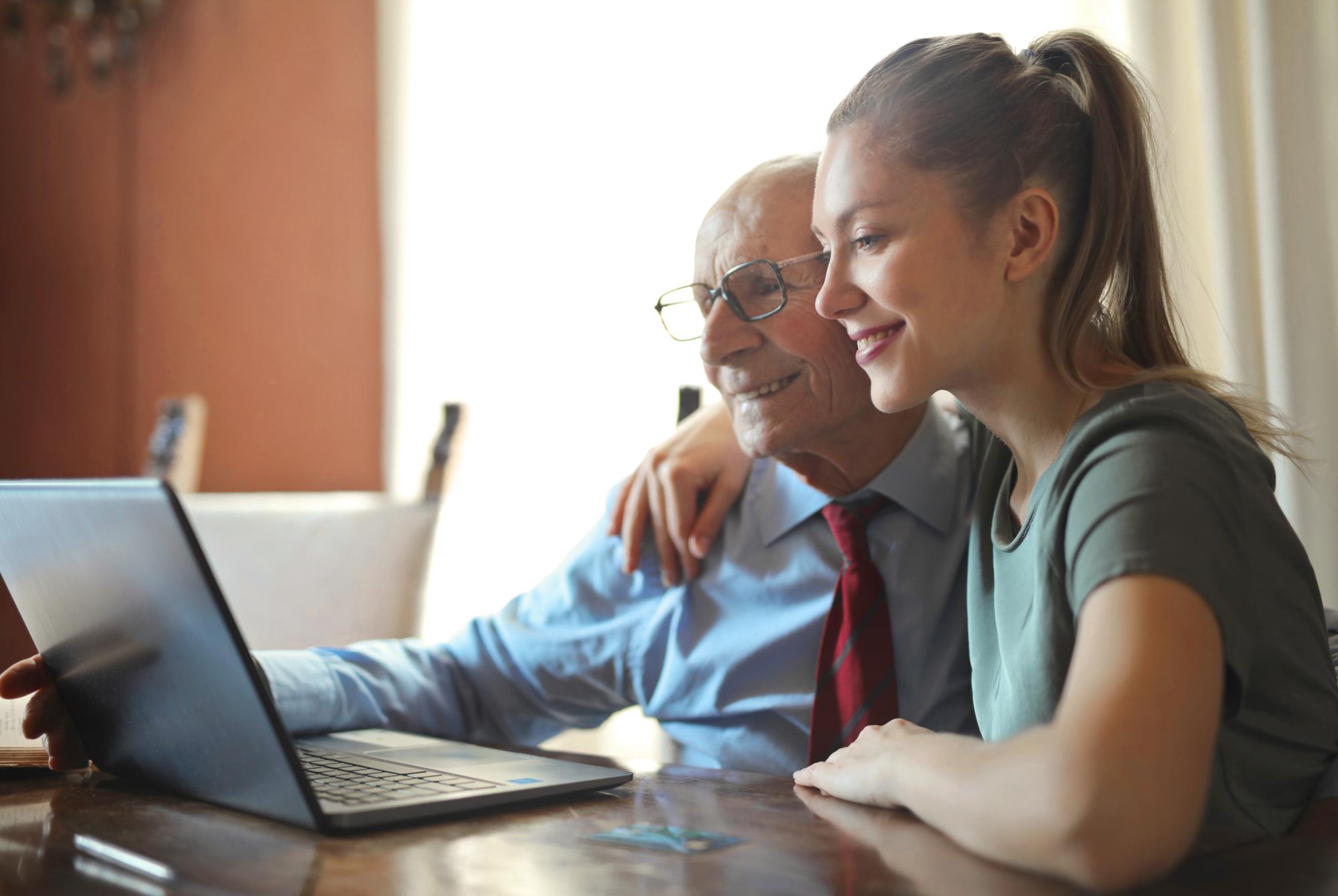 Elderly man on computer being helped by young woman