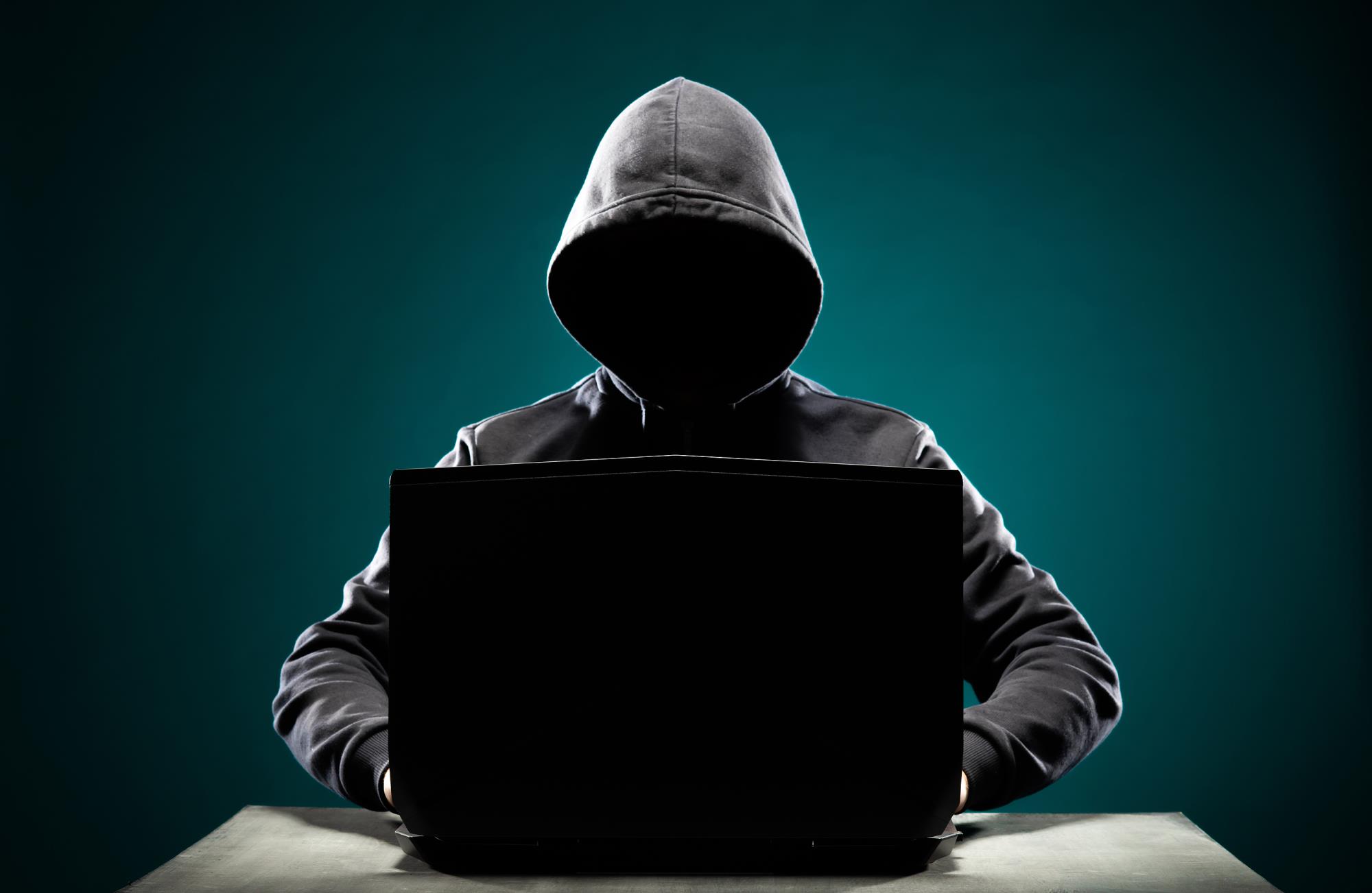 Hacker working on laptop in hoodie