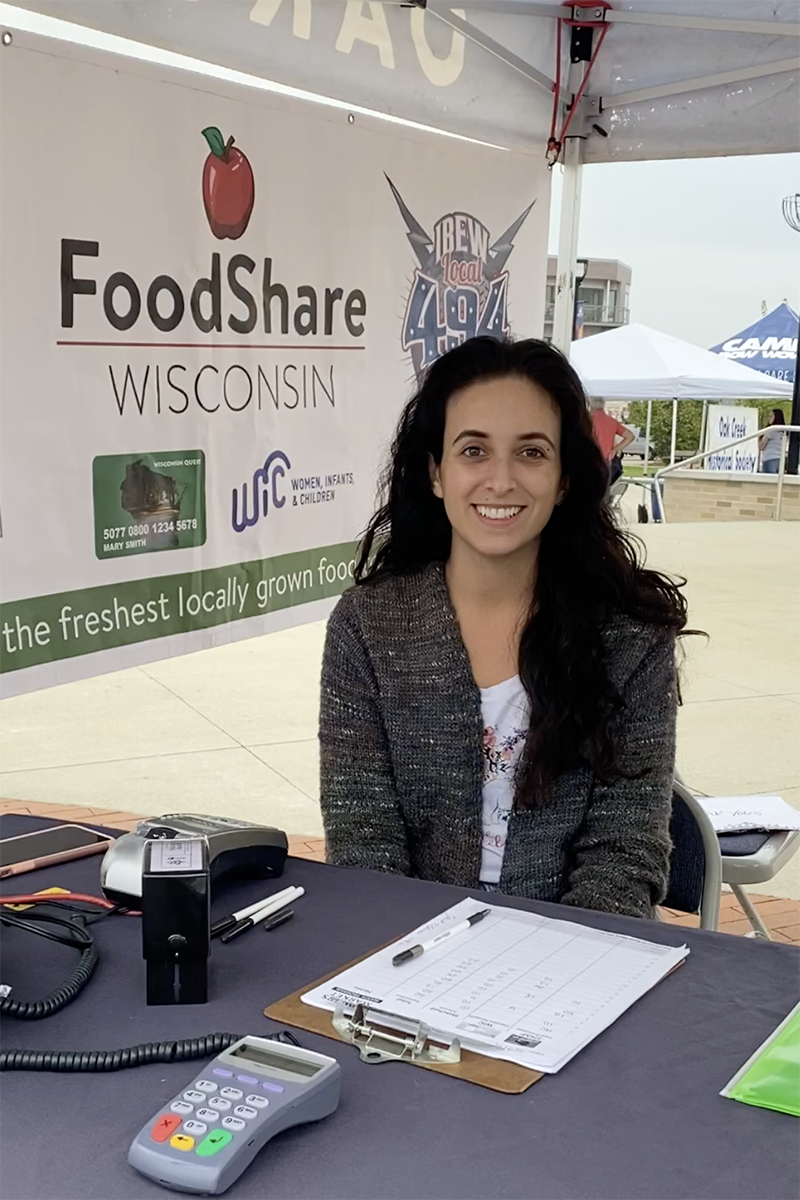 Dark-haired woman sitting in FoodShare tent