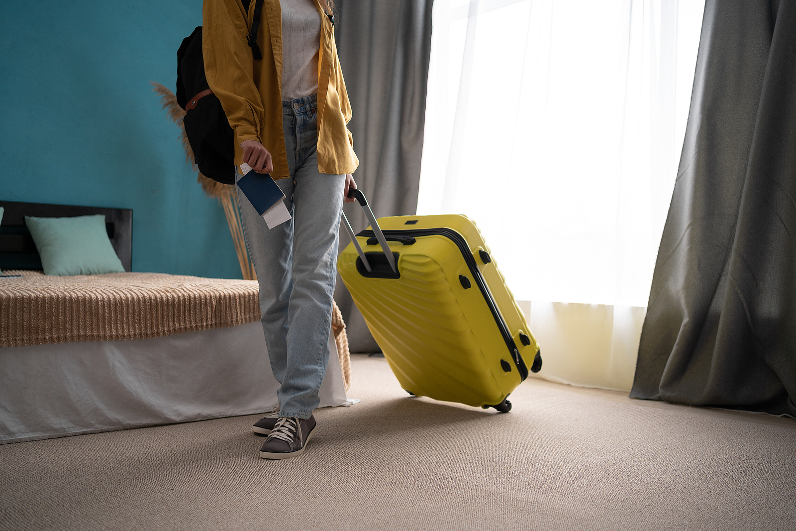 Hotel guest with a yellow suitcase walking away from window.