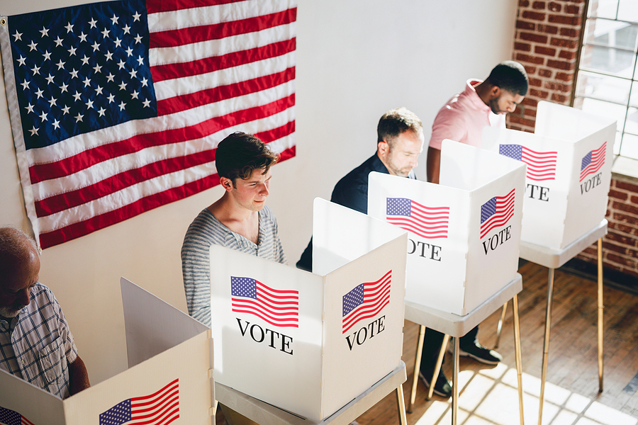 people voting in voting booths with a large American flag behind them